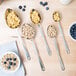 A spoon with cereal in it next to a bowl of cereal and blueberries.