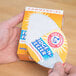 A hand holding a box of Arm & Hammer Fridge-N-Freezer Baking Soda.