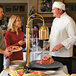 A chef carving meat at a hotel buffet using a Hatco carving station.