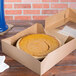 A Rustic Orange Window Pie Box with an Autumn Design containing a pie on a table in a bakery display.