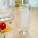 A Libbey tequila shooter glass filled with liquid next to a bottle of tequila with a lemon and a lime.