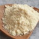 A wooden plate with a pile of Premium Gluten-Free Almond Flour next to a wooden spoon full of the flour.