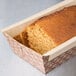 A loaf of bread in a Solut brown paper loaf pan on a table.