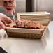 A person cutting a loaf of bread in a Solut cardboard loaf pan.