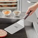 A person using a Mercer Culinary Hell's Handle spatula to cut meat on a grill.