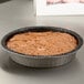 A brown cake in a Solut round paperboard cake pan on a table.