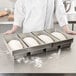 A woman in a white chef's coat holding a Chicago Metallic bread loaf pan filled with white dough.