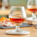 An Acopa brandy snifter filled with brown liquid on a table with a coaster.