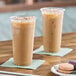 Two Choice clear plastic cups filled with iced coffee on a wooden table with cookies.