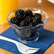 A clear plastic bowl of blackberries on a table with a napkin and a plastic fork.
