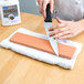A person sharpening a knife on a white block using a Victorinox India Fine Sharpening Stone.