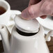 A person's hand pressing a white lid on a Homer Laughlin China Beverage Server.