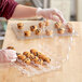 A person in gloves holding an InnoPak clear plastic container with mini cupcakes.