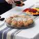 A clear plastic catering tray with a dome lid on a table filled with food.