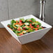 An American Metalcraft square porcelain bowl filled with salad on a table.