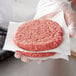 A person holding a raw hamburger patty wrapped in Choice patty paper.