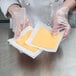 A person in a white coat wearing a plastic glove puts cheese on patty paper.