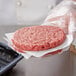 A hand holding a raw hamburger with a black container of Choice patty papers on a counter.