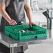 A woman in an apron holding a green Vollrath flatware rack filled with silverware.