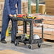 A man standing next to a Rubbermaid utility cart with tools on it.