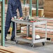 A man in a blue jumpsuit and hard hat standing next to a Rubbermaid utility cart with tools on it.