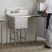 A man standing next to a Regency stainless steel commercial sink with a right drainboard.