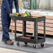 A man in blue overalls standing next to a Rubbermaid utility cart with tools.