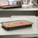 A brown cake in a Solut paperboard pan with clear lid on a counter.