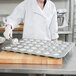 A woman in a white coat using a Chicago Metallic muffin pan to bake.