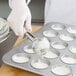 A person using a pastry scoop to fill a Chicago Metallic cupcake tin with white batter.