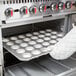 A person putting a Chicago Metallic muffin pan with muffins into an oven.