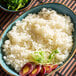 A bowl of cooked medium grain white sushi rice garnished with sliced vegetables and greens.