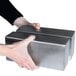 A pair of hands holding two rectangular stainless steel metal blocks.