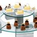 An Eastern Tabletop round acrylic display shelf with cakes on it.