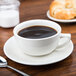 A CAC ivory china cappuccino cup on a saucer with a spoon and a croissant.