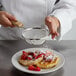 A person using a Tablecraft fine tin mesh strainer to sprinkle powdered sugar on waffles with strawberries.