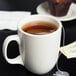 A CAC ivory china mug filled with tea and a tea bag on a plate.
