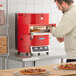 A person putting pizza in a red TurboChef countertop oven.