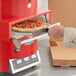 A person using a TurboChef Fire pizza oven to cut a pizza.