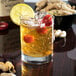 A Libbey rocks glass of whiskey with ice and lemon slices and cherries.
