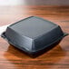 A Dart black foam square take out container on a wood surface.
