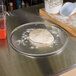 A dough ball on an American Metalcraft aluminum pizza pan on a table.