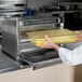 A person in a white coat placing a container of food in an Amana commercial steamer microwave.