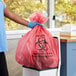 A person wearing gloves holding a red biohazard bag.