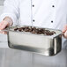 A person holding a Master-Bilt stainless steel gelato pan filled with ice cream.