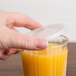 A hand using a Dinex translucent plastic lid to cover a glass of orange juice.