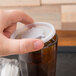 A hand using a Dinex translucent plastic lid on a glass of liquid.