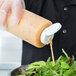 A clear 24 oz. squeeze bottle with a white flip lid being used to pour dressing onto a salad.