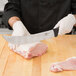 A person in gloves holding a Victorinox Cimeter knife over raw meat.