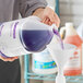 A person pouring lavender purple liquid into a white gallon jug.